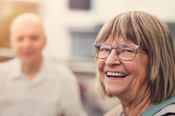 elderly woman smiling at café blurred man in background