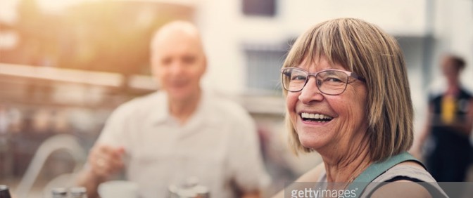 elderly woman smiling at café blurred man in background