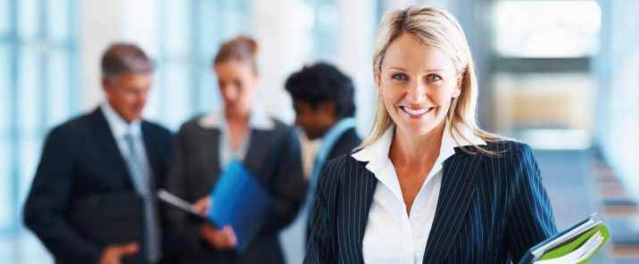 woman in suit smiling holding green folder people in background