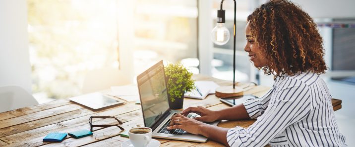 Woman using laptop at wooden desk with coffee and plant