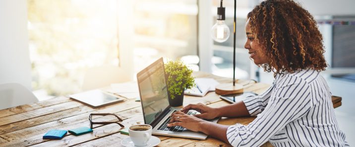 Woman using laptop at wooden desk with coffee