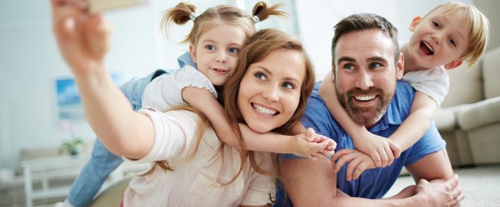 parents taking selfie with two young children on floor