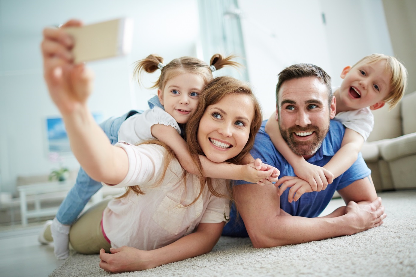 parents taking selfie with two young children on floor
