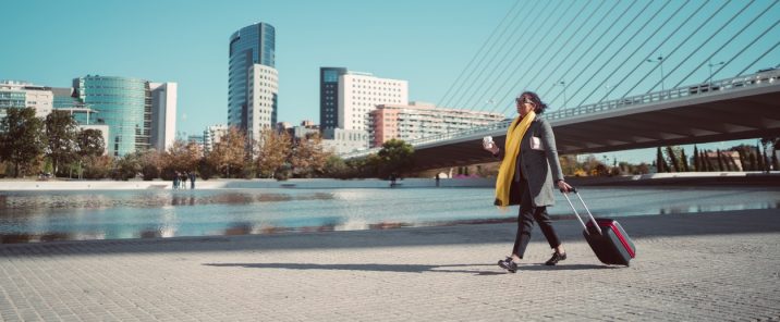 woman holding cup carying suitcase outside