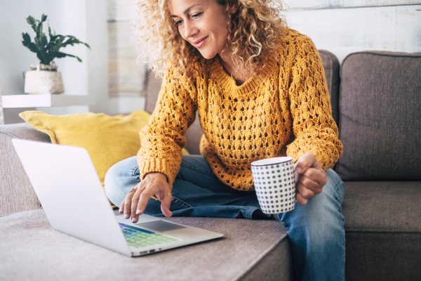 woman sitting on sofa using macbook holding mug