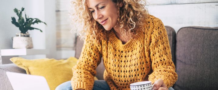 woman sitting on sofa using macbook holding mug