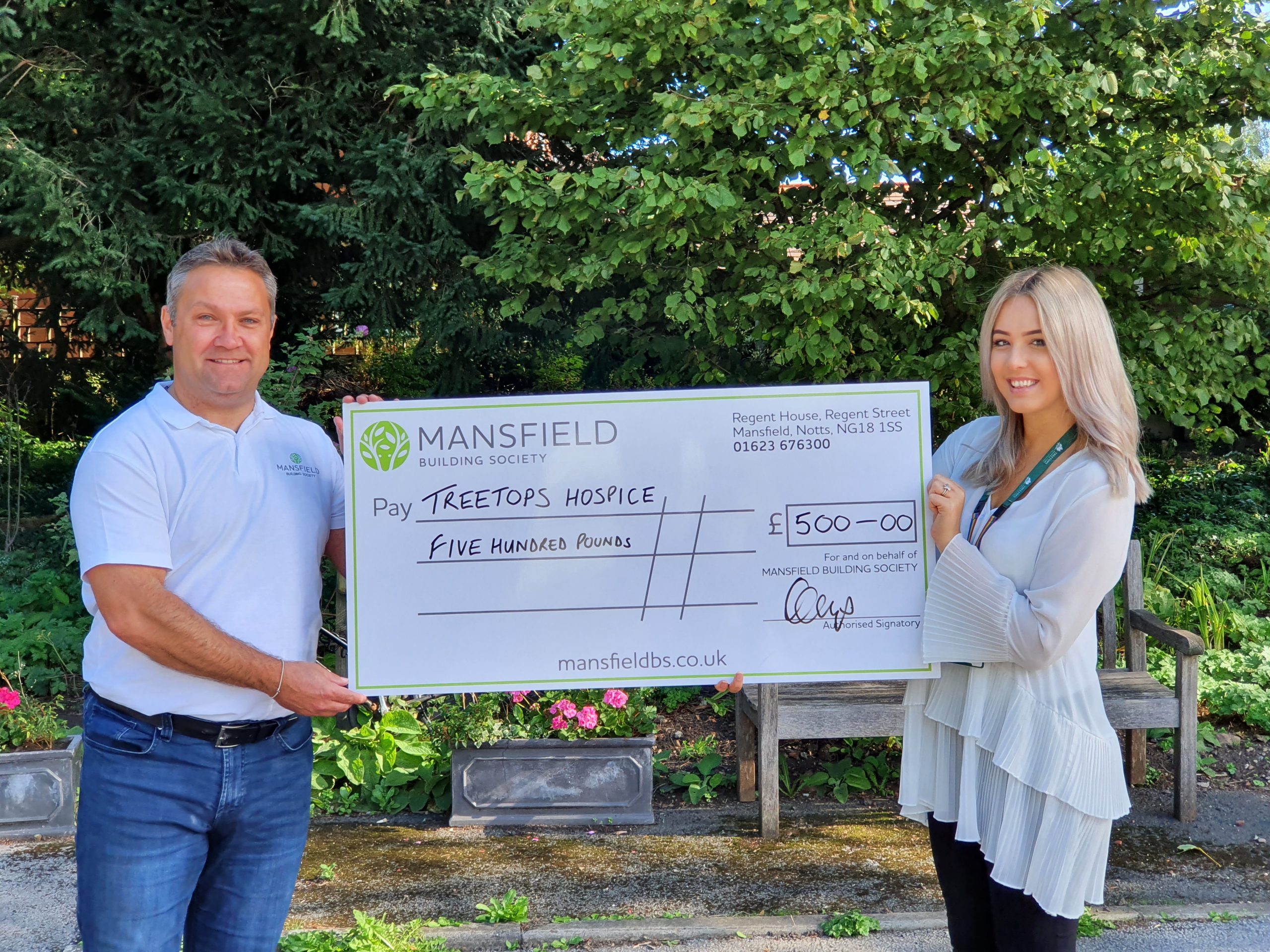 Treetops hospice man and woman holding mansfield cheque outside