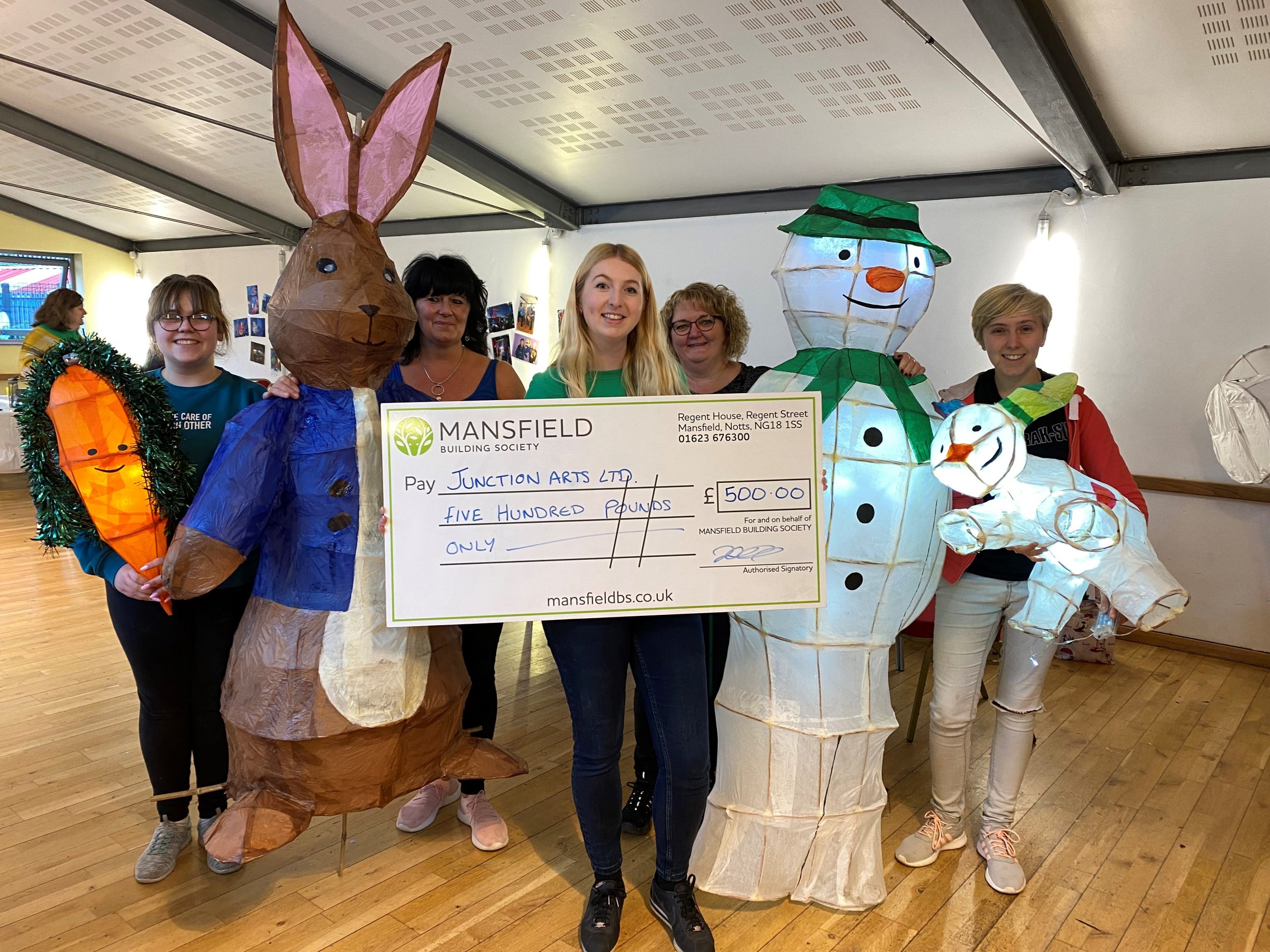 Women holding bunny and snowman lanterns with large cheque