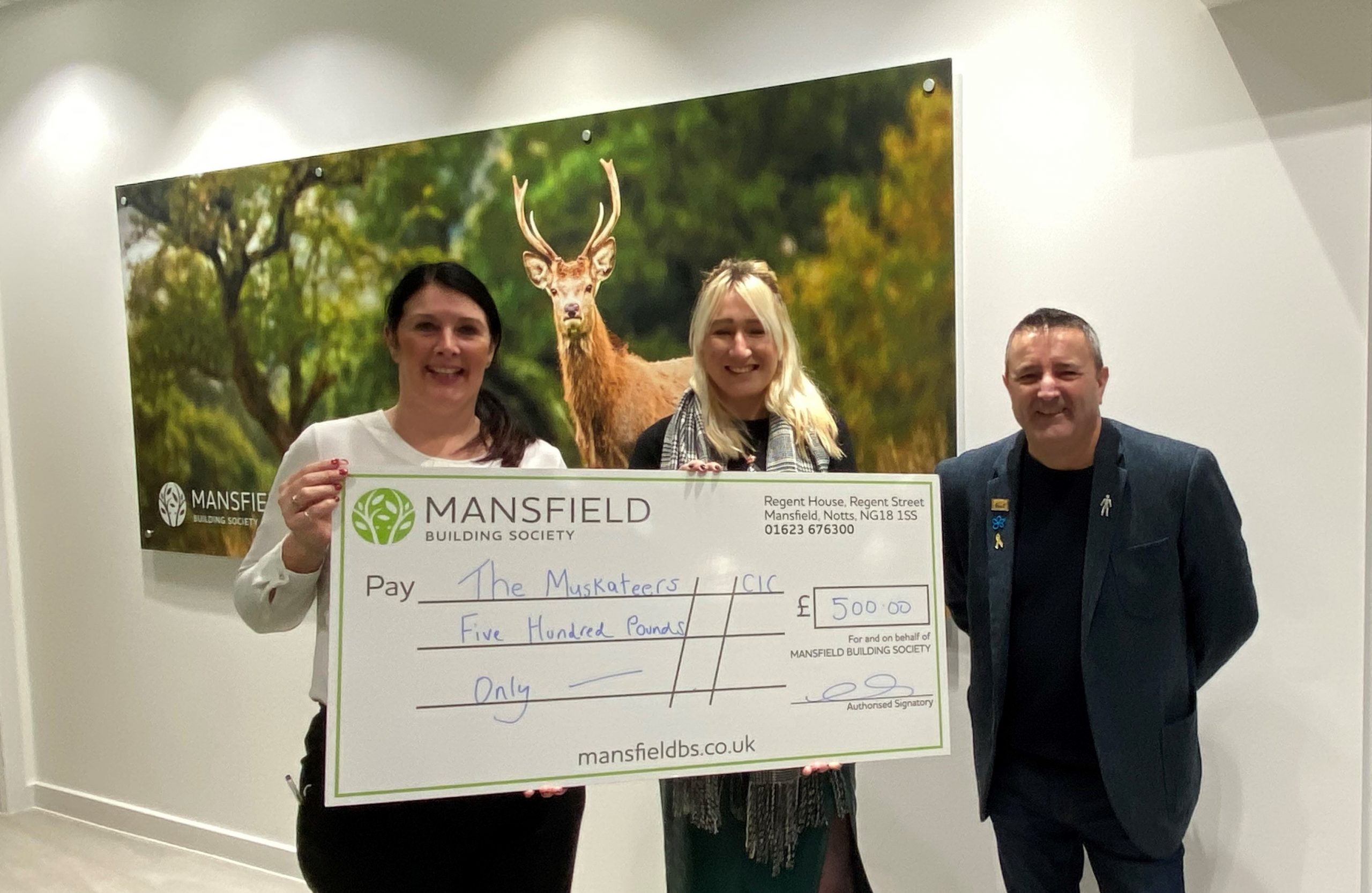 Man and two women holding mansfield bs cheque in front of deer image