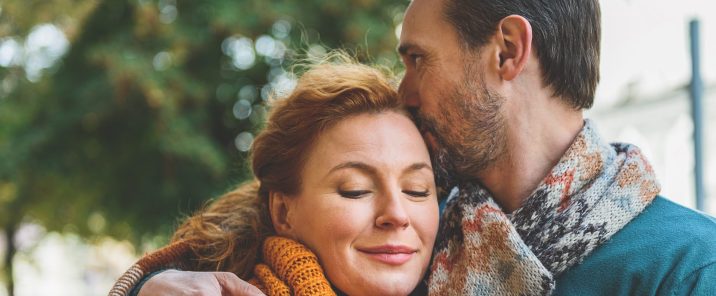 A middle-aged couple cuddle under a blanket outdoors